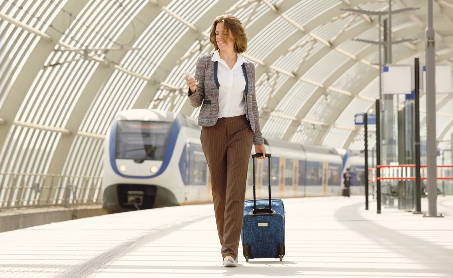Woman walking with her suitcase looking at her phone
